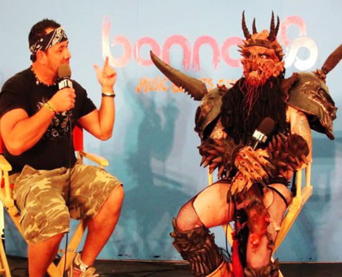 Moe Train interviewing Dave Brockie as Oderus Urungus of GWAR on a stage at Bonnaroo, both holding Moe Train's Tracks mics
